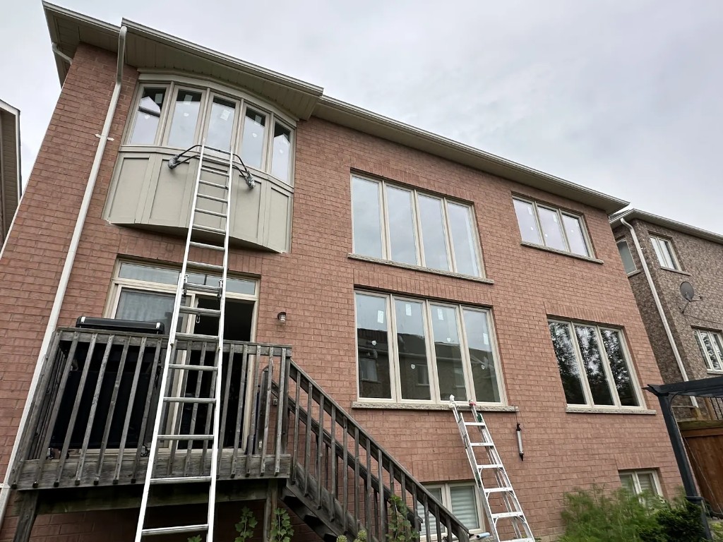 Brick home with new windows, a bay window, and ladders set for installation