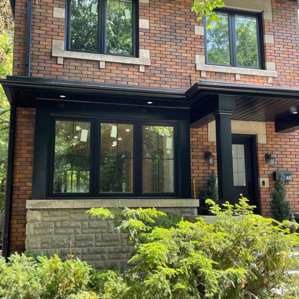 Brick home with black-framed security windows and covered front entrance surrounded by greenery