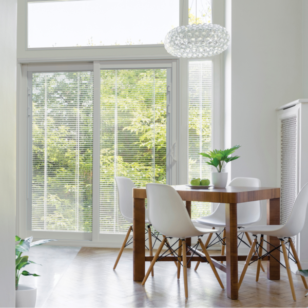 Sliding glass door with white blinds beside a wooden dining table and white chairs in a bright room