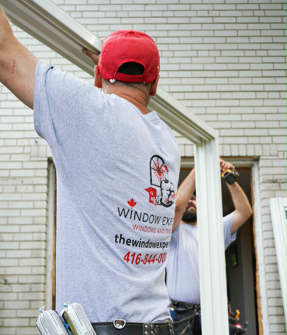Window Experts installers wearing tool belts fitting a white window frame into a brick house