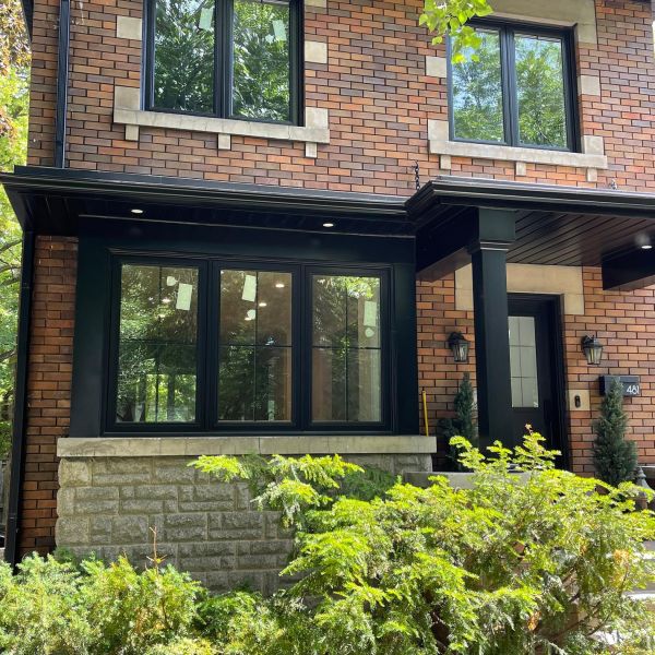 Brick home with black-framed security windows and covered front entrance surrounded by greenery